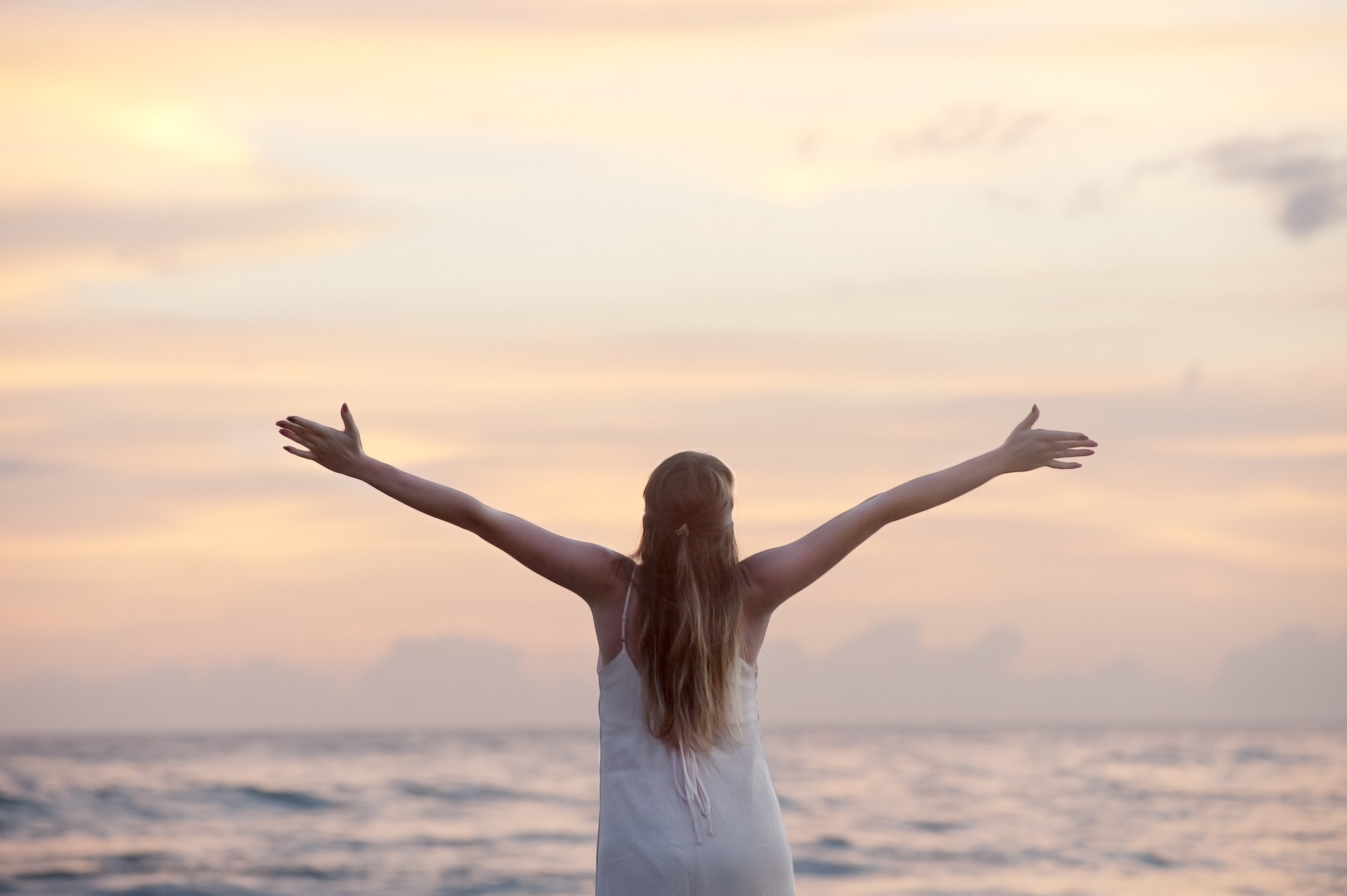 Mujer al atardecer con los brazos abiertos frente al mar